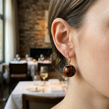 Kolczyk ze złotym zapięciem i brązowo-czarną kulką na modelce w restauracji